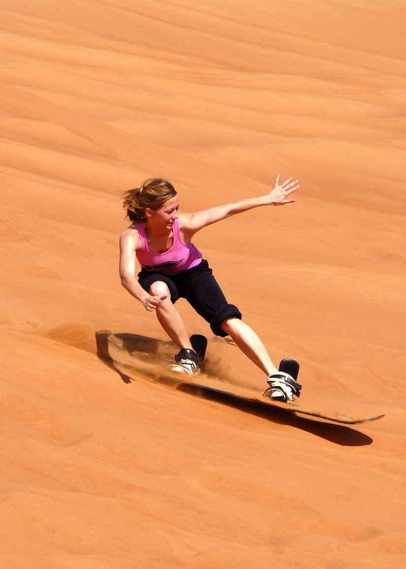 Awesome bucket list ideas — a woman sandboarding over sand dunes, dubai.