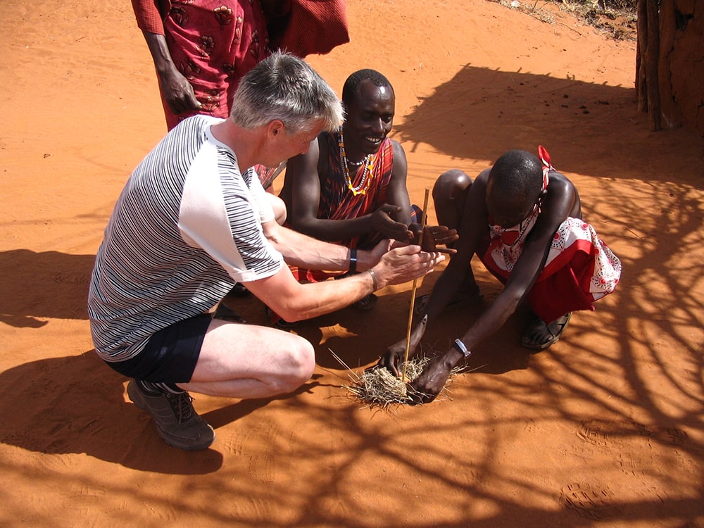 G adventures tour review — maasai people and a tourist lighting a fire in a village on the a109 road, kenya.