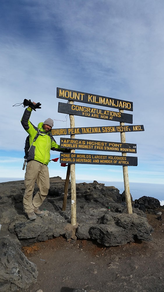 Kilimanjaro routes review — man standing beside the mount kilimanjaro summit sign.